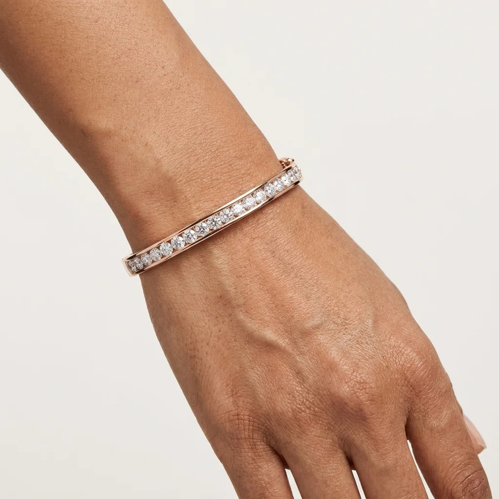 A close-up of a person's wrist wearing a slim pavé bracelet in rose gold with clear stones, set against a plain light background.