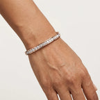 A close-up of a person's wrist wearing a slim pavé bracelet in rose gold with clear stones, set against a plain light background.