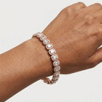A rose gold tennis bracelet with radiant-cut clear diamonds, shown worn on a person's wrist against a light gray background.