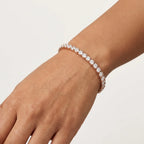 A close-up of a person's wrist wearing a rose gold tennis bracelet with clear round-cut diamonds, set against a clean, light off-white background.