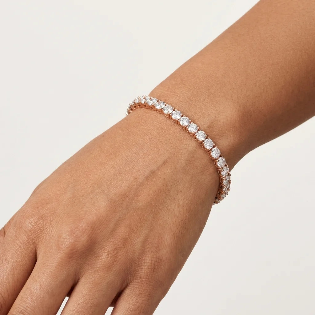 A close-up of a person's wrist wearing a rose gold tennis bracelet with clear round-cut diamonds, set against a clean, light off-white background.