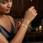 A woman wearing a delicate rose gold tennis slider bracelet with small clear stones, shown in a warm, dimly lit indoor setting.