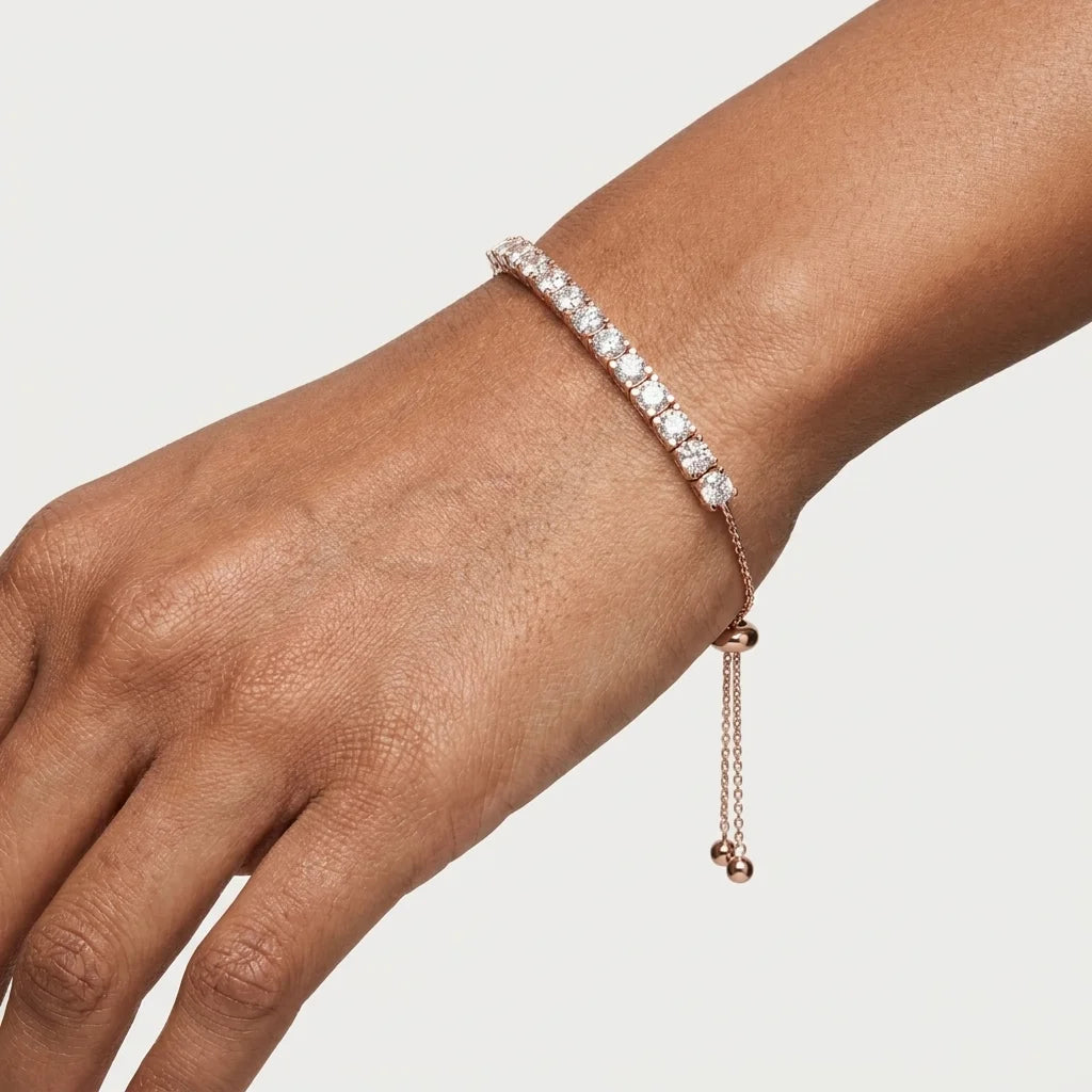 A woman wearing a delicate rose gold tennis bracelet with clear diamonds, shown in a close-up portrait against a dark, elegant background.