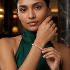 A woman wearing a delicate diamond bracelet on her wrist, dressed in a dark green high-neck top, set against a softly blurred indoor background with warm lighting.