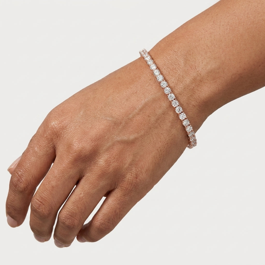 A close-up of a person's wrist wearing a delicate diamond tennis bracelet on a light gray background.