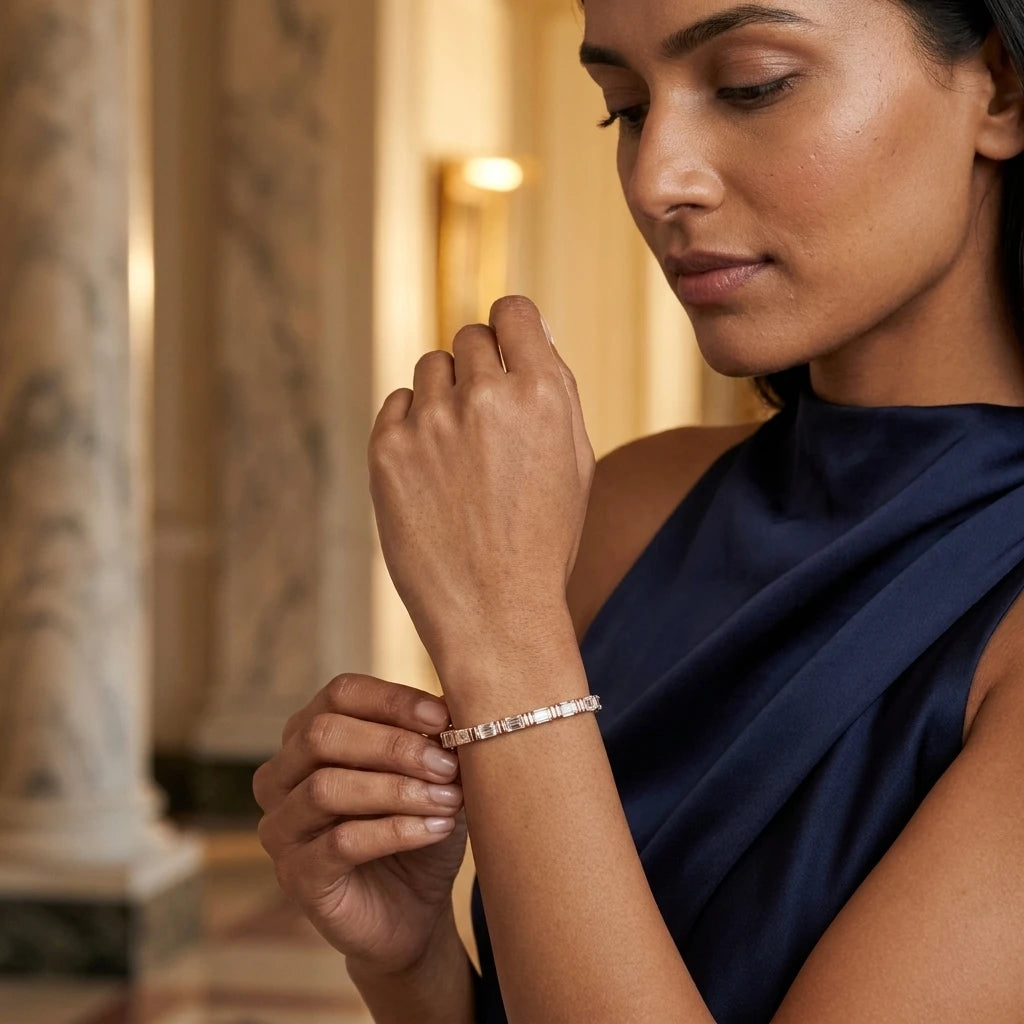 A close-up lifestyle shot of a woman wearing a delicate rose gold tennis bracelet with small clear diamonds, resting her arm on a dark velvet surface.