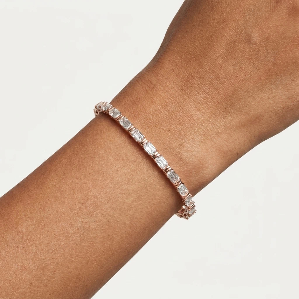 A close-up of a rose gold tennis bracelet with clear emerald-cut diamonds worn on a person's wrist against a clean off-white background.