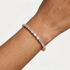 A close-up of a rose gold tennis bracelet with clear emerald-cut diamonds worn on a person's wrist against a clean off-white background.
