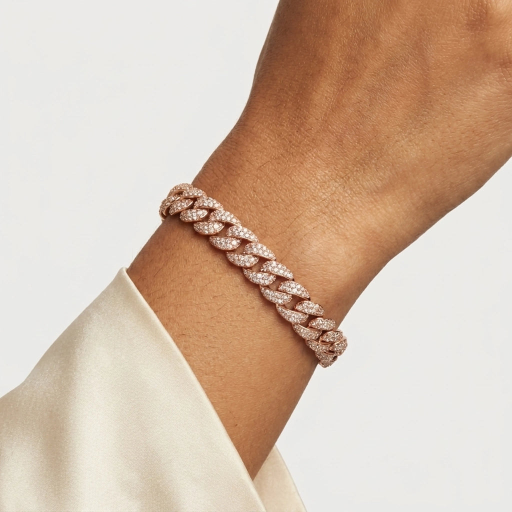 A close-up of a person's wrist wearing a rose gold Cuban link bracelet paved with small clear diamonds, paired with a cream-colored satin sleeve.