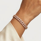A close-up of a person's wrist wearing a rose gold Cuban link bracelet paved with small clear diamonds, paired with a cream-colored satin sleeve.