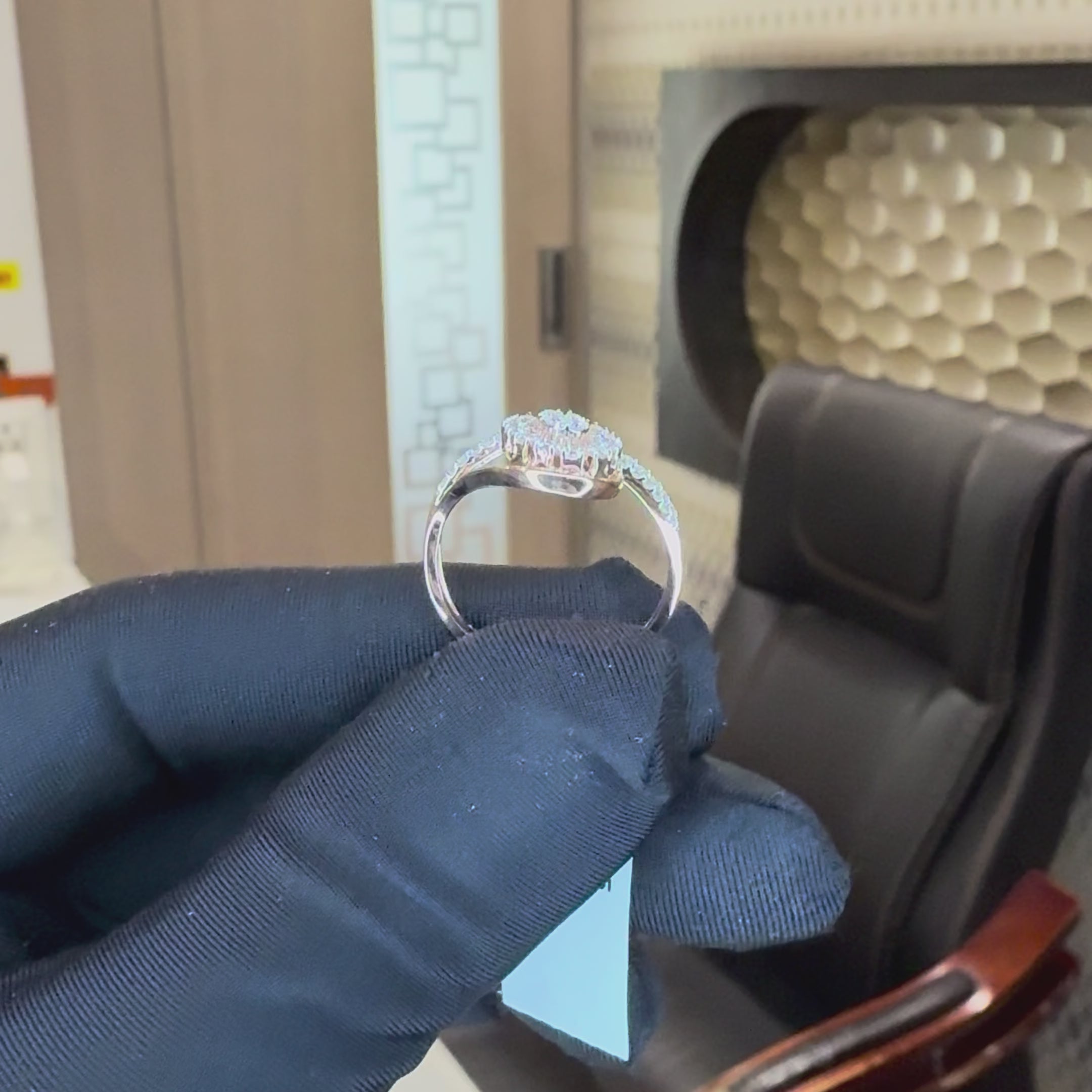 Rose gold ring with diamond accents is holding by a hand which is worn black gloves and showing the ring from every angle by tilting the hand and bringing closer hand to show the ring clearly against the neutral background.