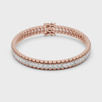 Rose gold bracelet with emerald diamond accents on a white surface is rotating parallel to the surface.