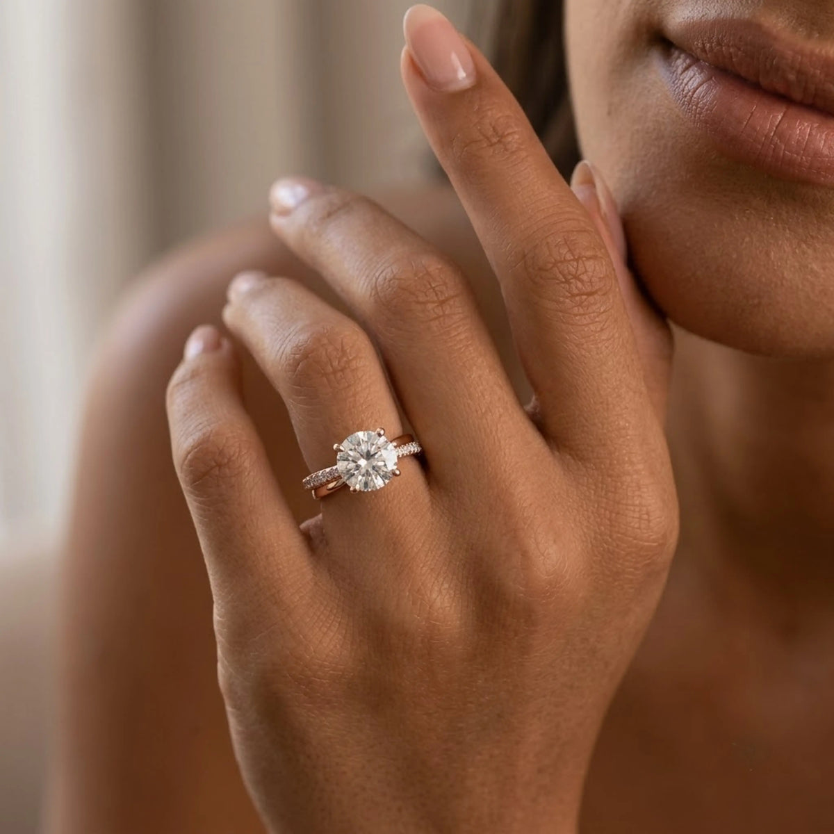 Woman wearing a rose gold solitaire engagement ring with a round brilliant cut diamond and pavé-set band, photographed in warm, soft lighting.