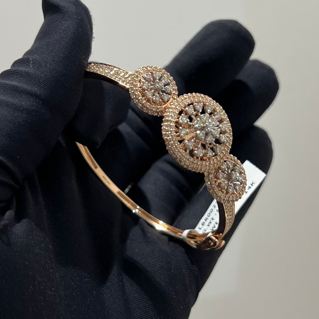 Gold and diamond bracelet held by a gloved hand on a neutral background