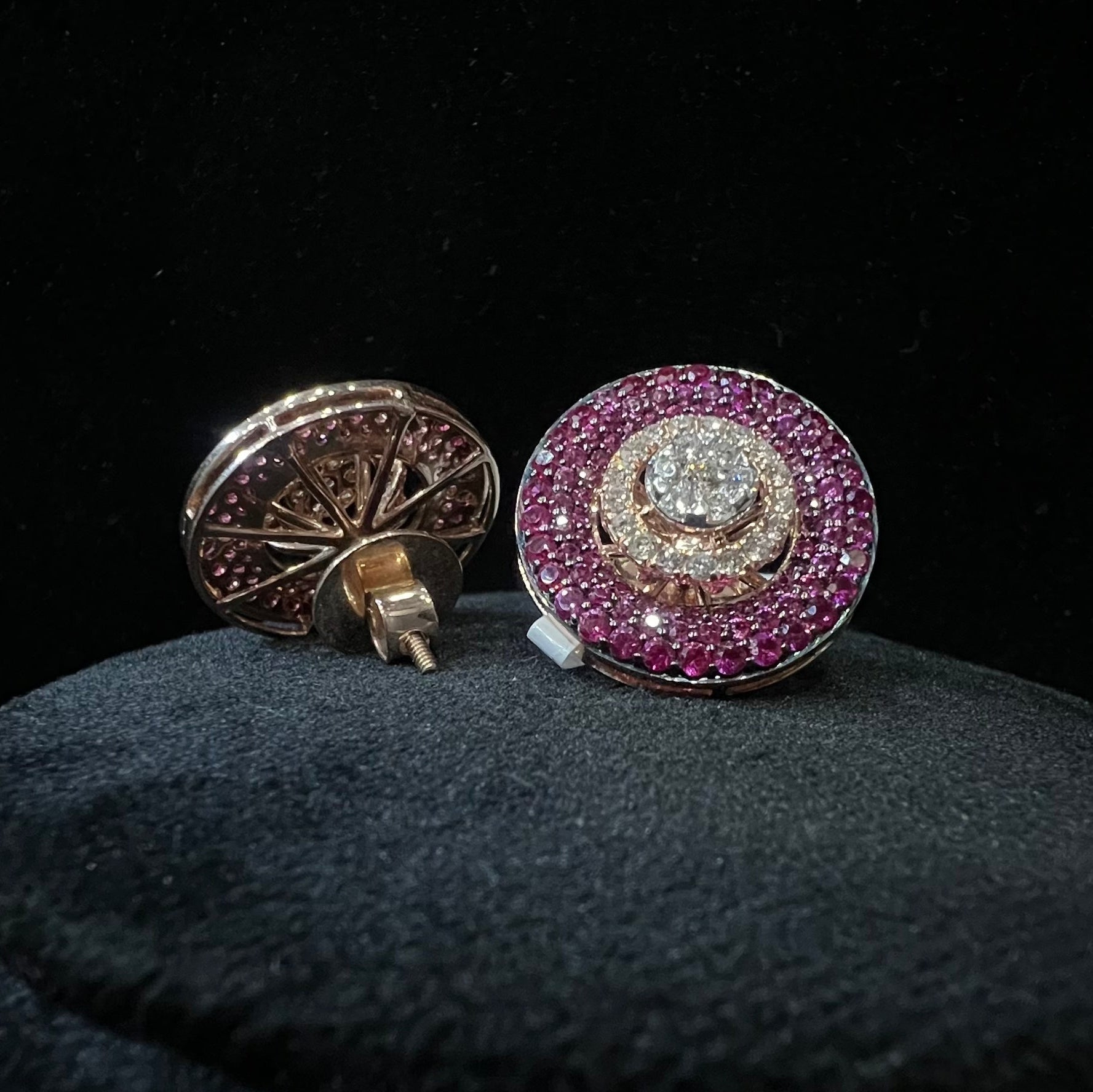 Pair of round diamond earrings with pink gemstones on a dark background