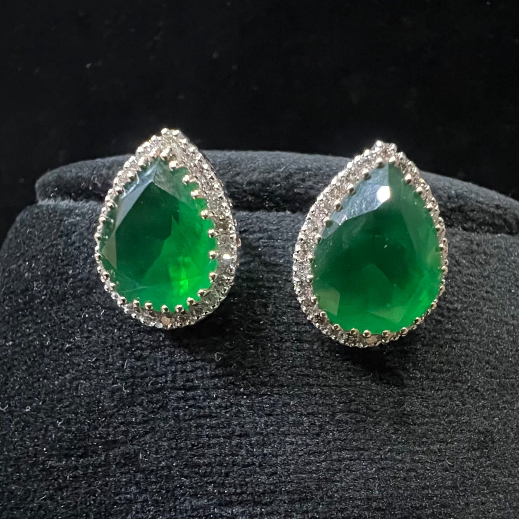 Pair of green teardrop earrings with diamond accents on a black stand.