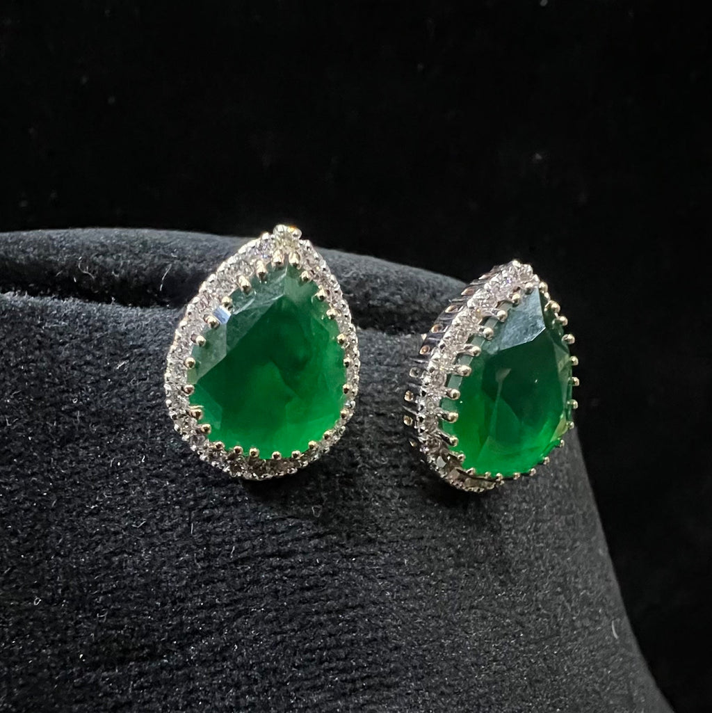 Green teardrop earrings with diamonds accents on a black velvet stand.