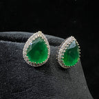 Green teardrop earrings with diamonds accents on a black velvet stand.