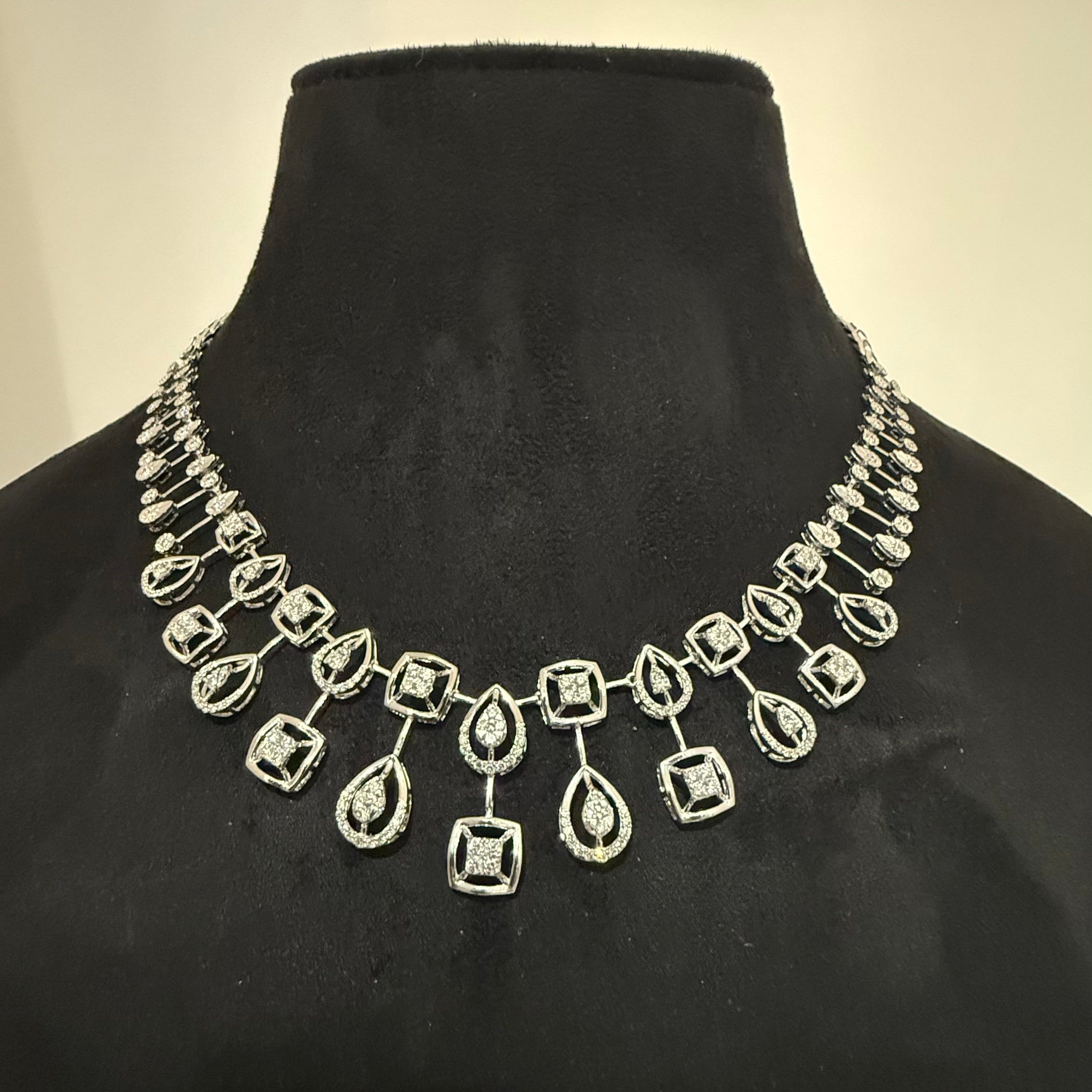 Gold diamond necklace and earrings on a black mannequin bust with a neutral background