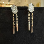 Pair of diamond earrings with hexagonal design on a black stand.
