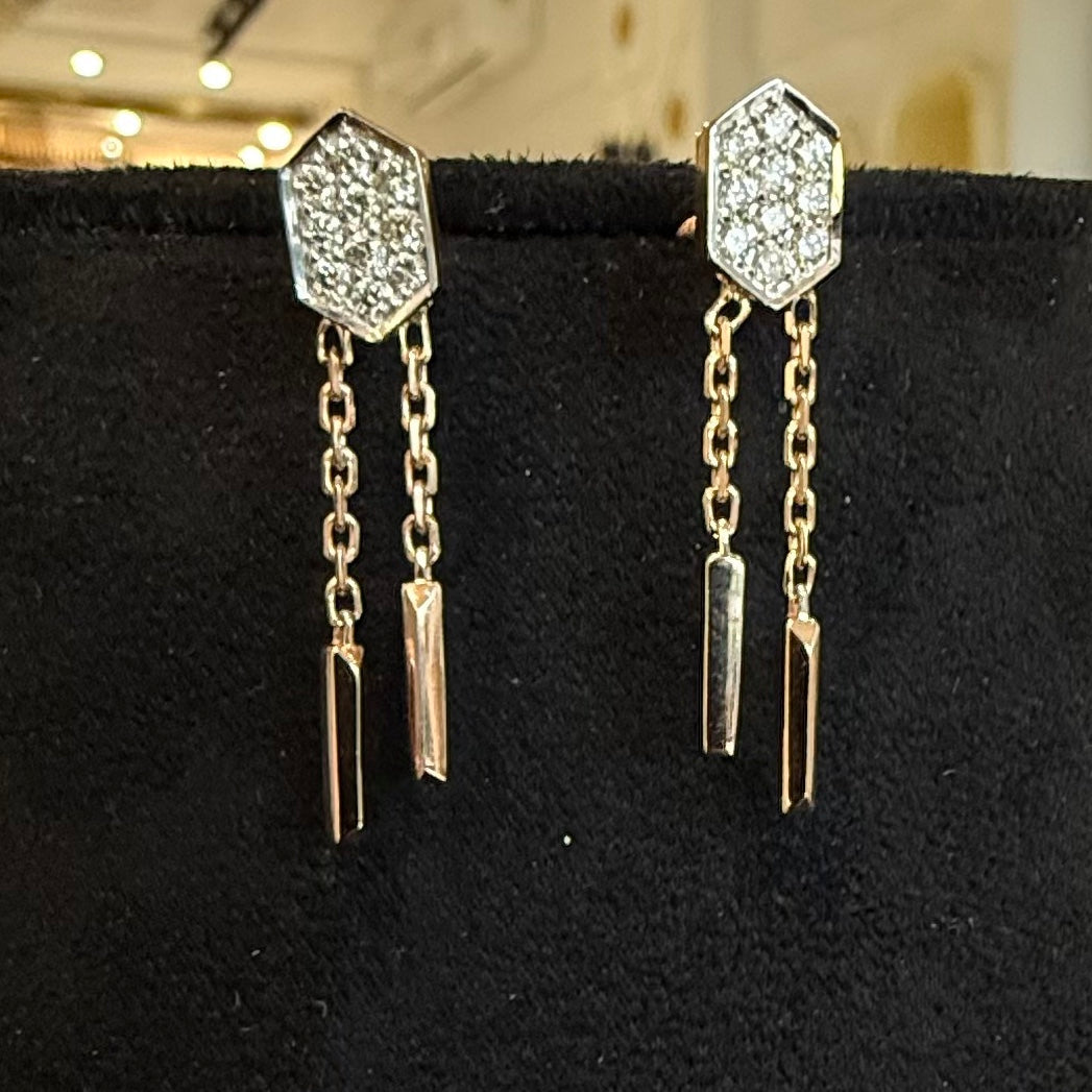 Pair of diamond earrings with hexagonal design on a black stand.