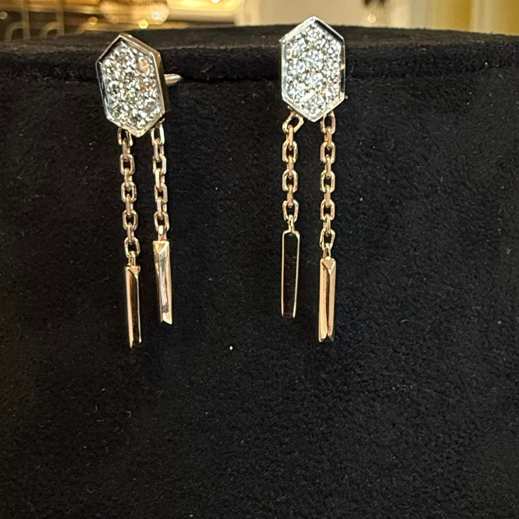 Pair of diamond earrings with chain and geometric design on a black stand.