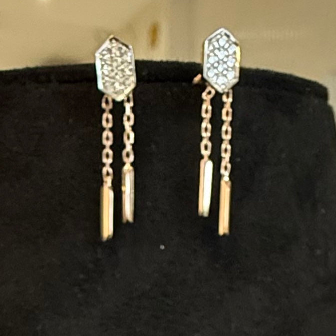 Gold earrings with chain and geometric design on a black stand.