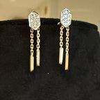 Gold earrings with chain and geometric design on a black stand.