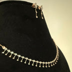 Gold diamond necklace and earrings on a black stand with a beige background