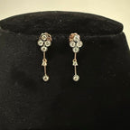 Pair of floral diamond earrings with dangling elements on a black velvet stand.