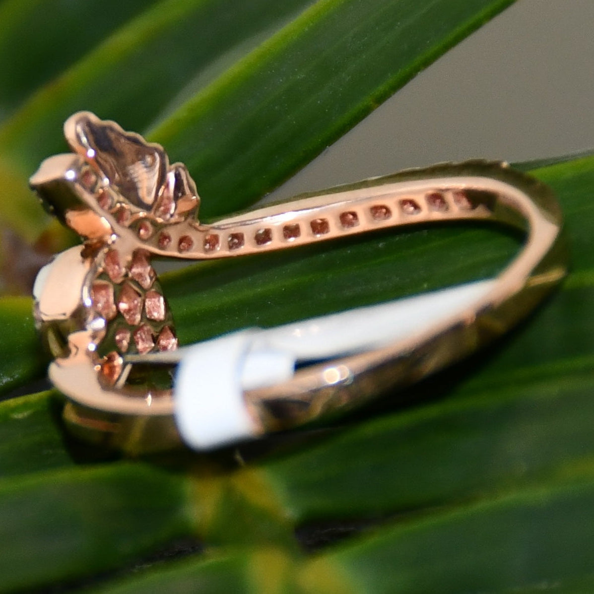 Rose gold ring with diamonds on a green leaf