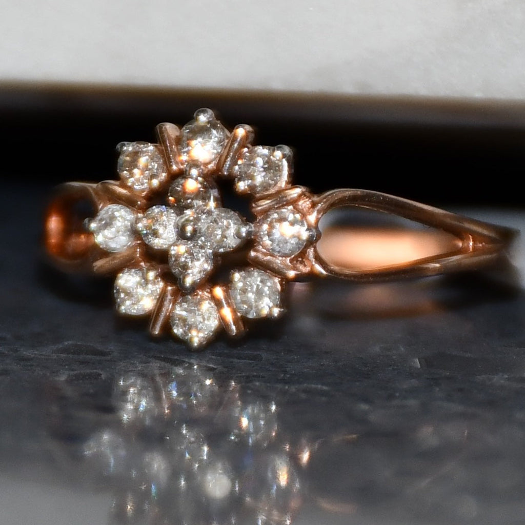 Rose gold ring with diamond flowers on a reflective surface