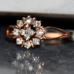 Rose gold ring with diamond flowers on a reflective surface