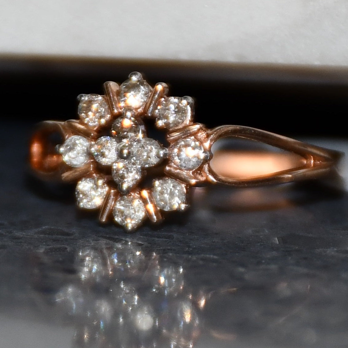 Rose gold ring with diamond flowers on a reflective surface