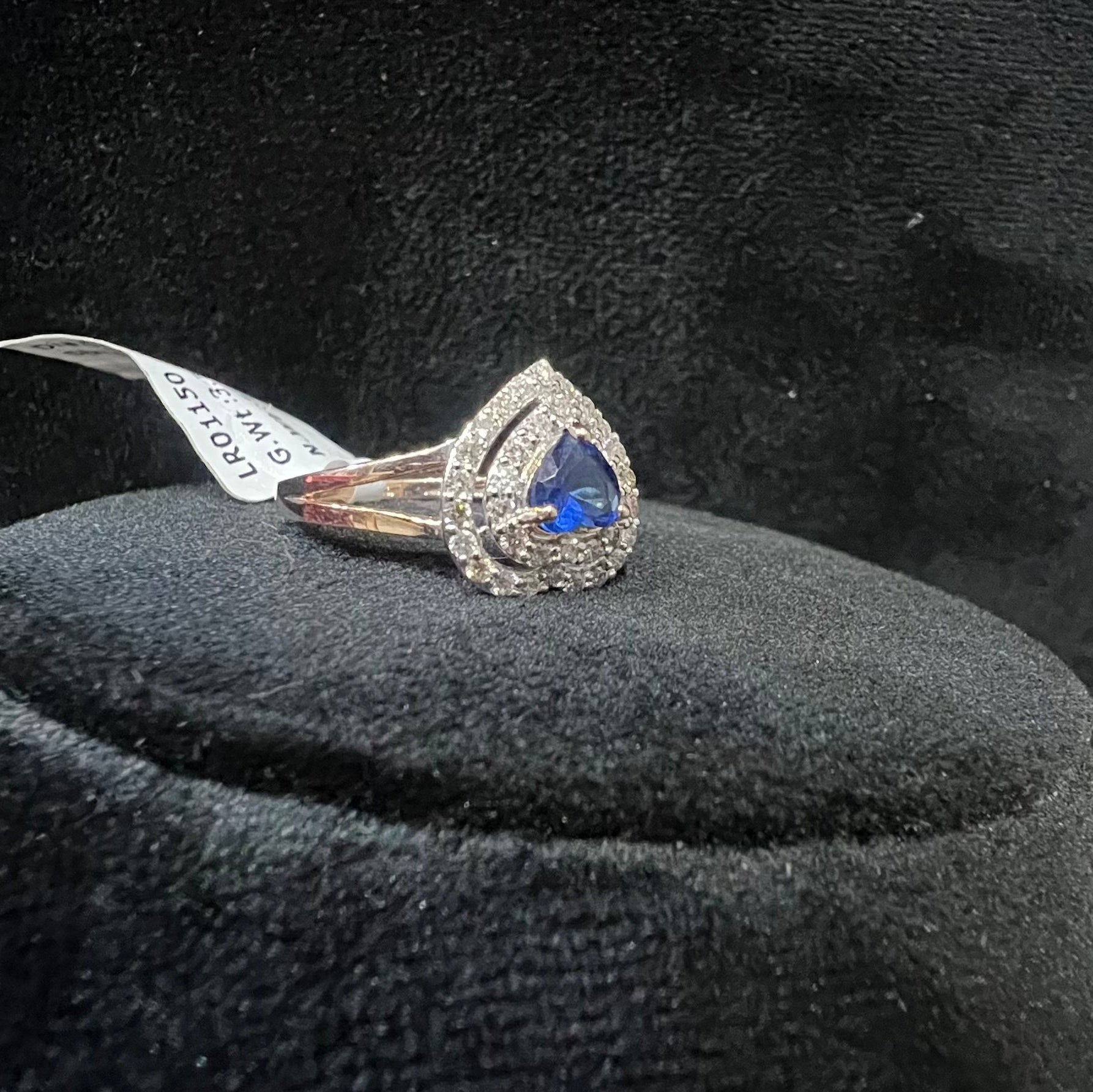 Gold diamond ring with a blue gemstone on a black velvet cushion