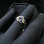 Ring with a blue gemstone and diamond accents held by a gloved hand against a black background