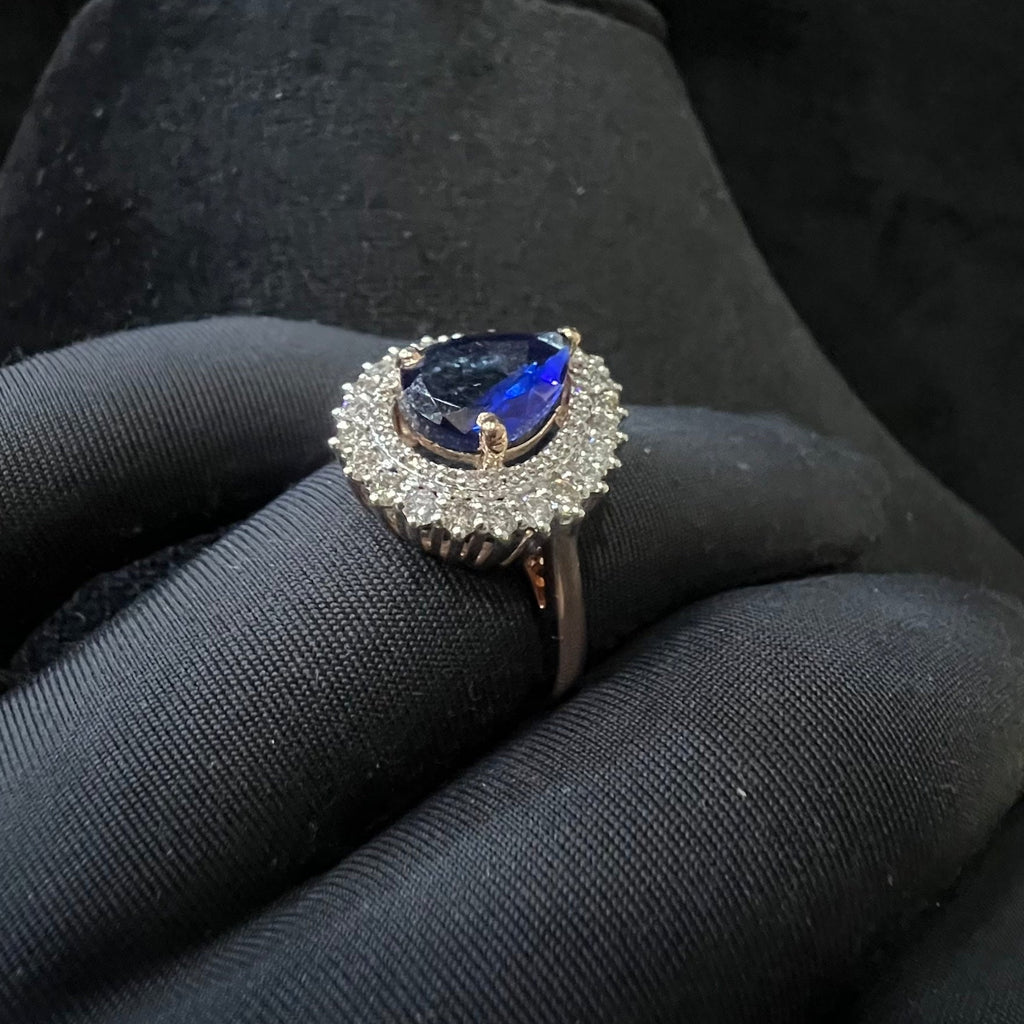Ring with a blue gemstone and diamond halo on a black glove
