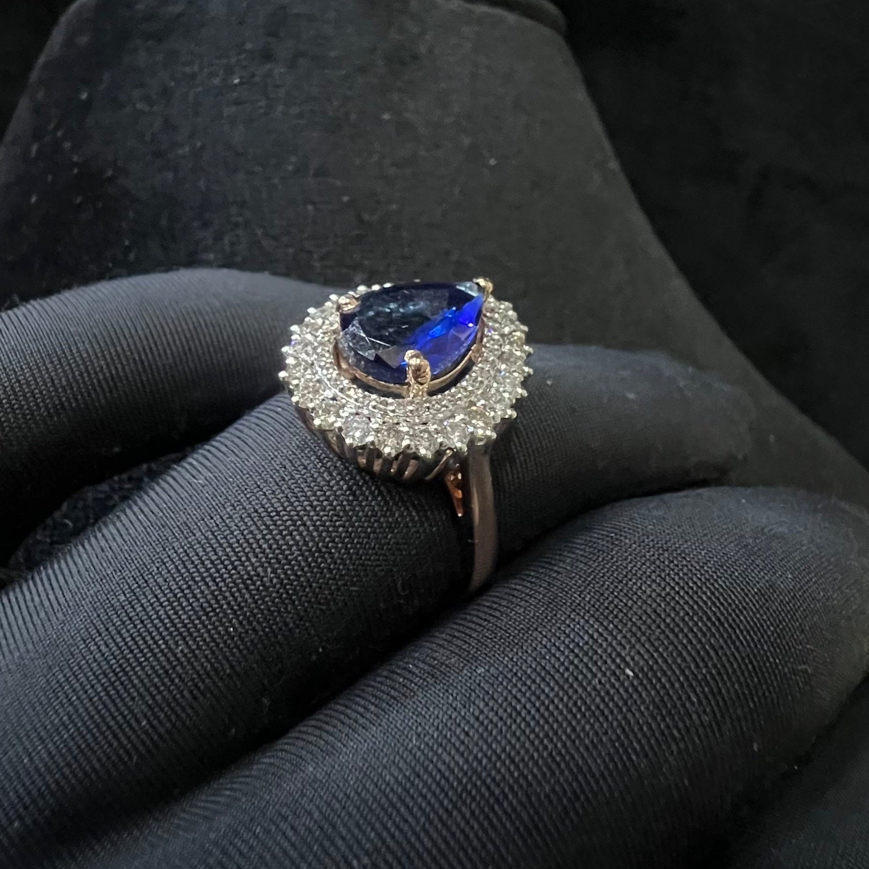 Ring with a blue gemstone and diamond halo on a black glove