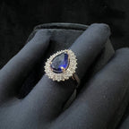 Gold ring with a blue gemstone and diamond accents on a black glove