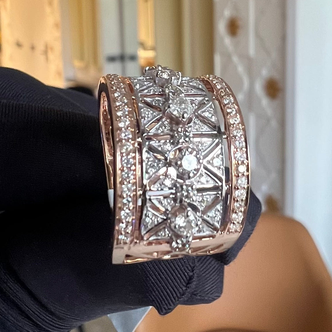 Gold ring with diamond accents held by a gloved hand.