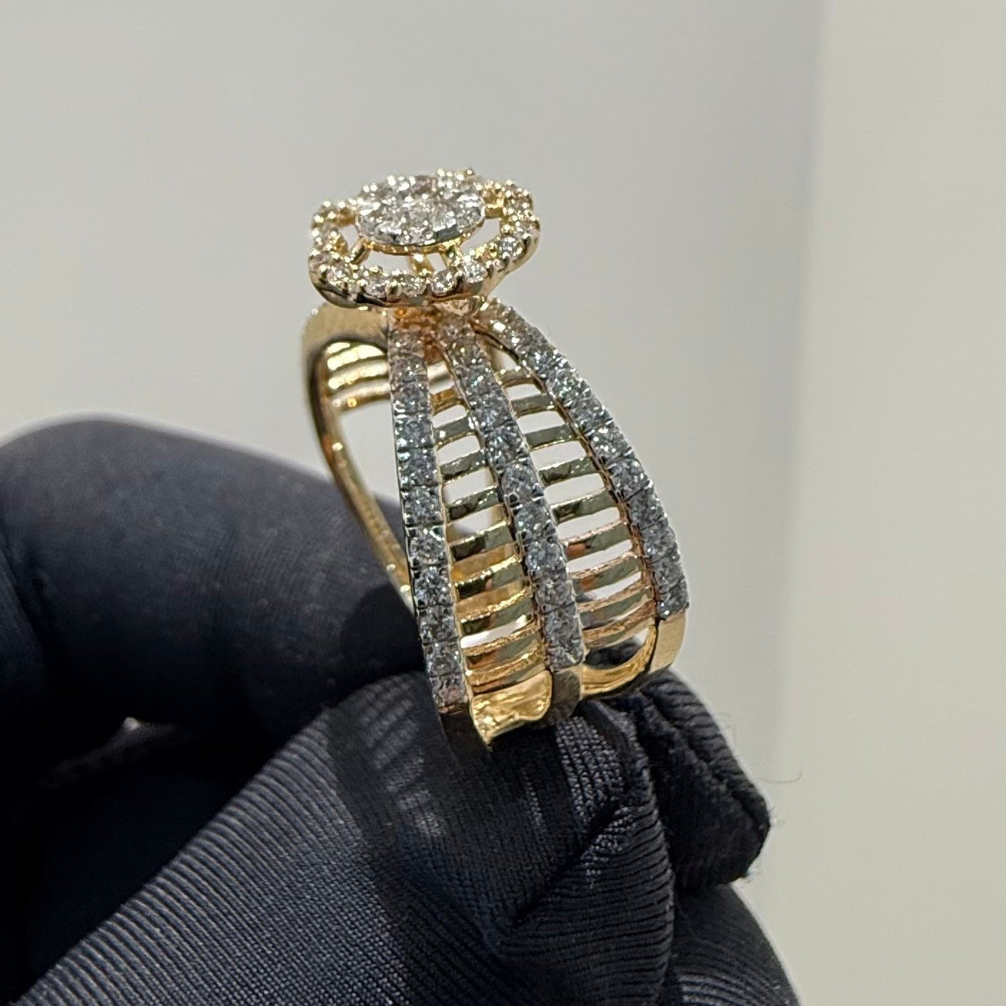 Gold and diamond ring held by a gloved hand against a neutral background
