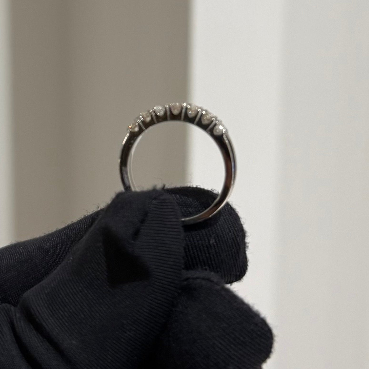 Gold ring held by a gloved hand against a neutral background