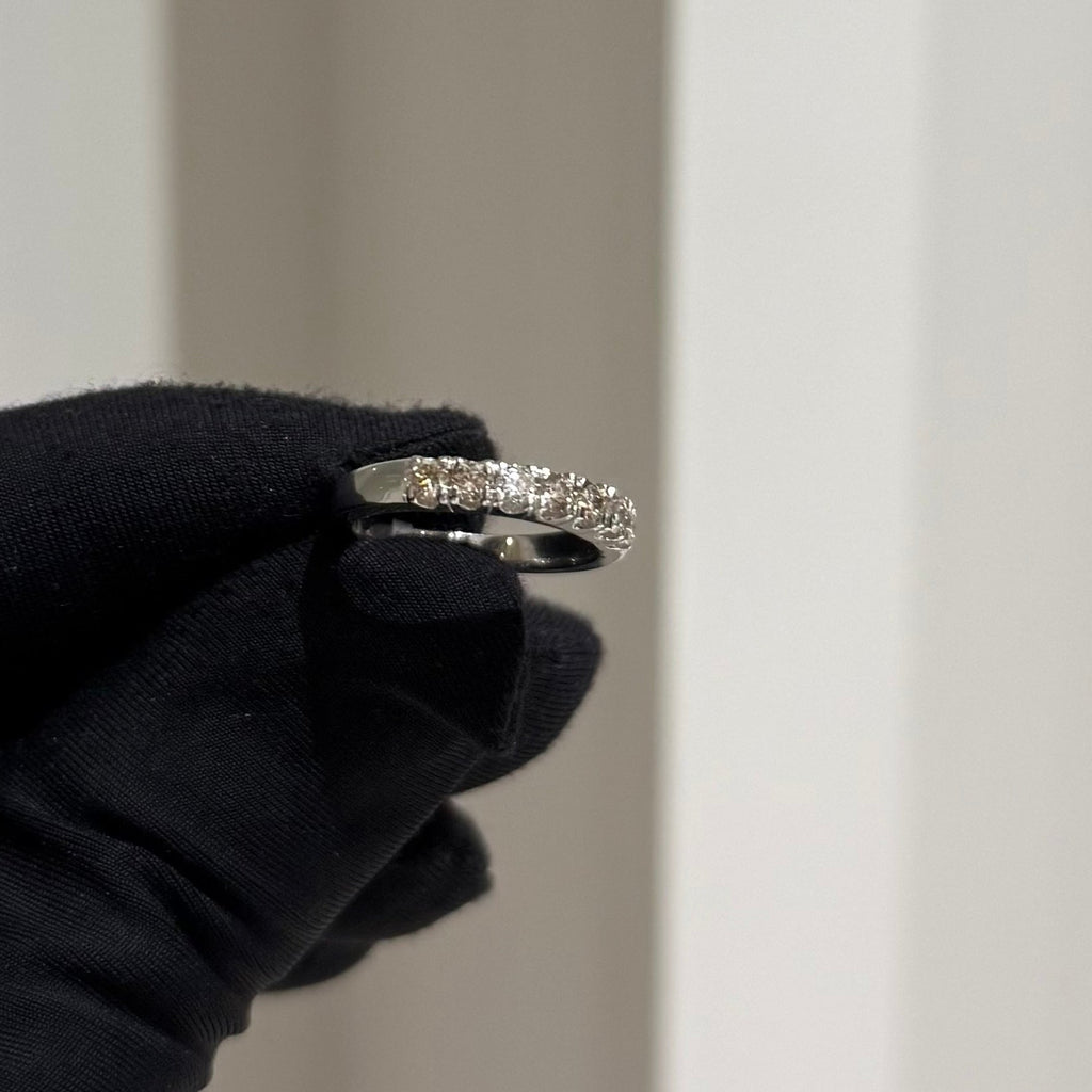 Gold ring with diamonds held by a gloved hand against a neutral background