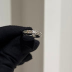 Gold ring with diamonds held by a gloved hand against a neutral background