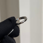 Gold ring with diamonds held by a gloved hand against a neutral background