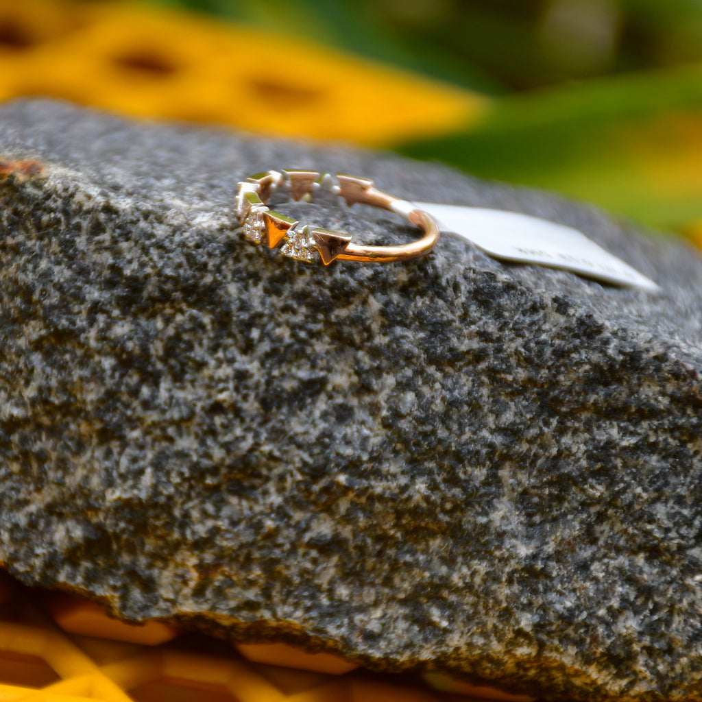 Gold diamond ring on a textured stone surface with blurred yellow flowers in the background