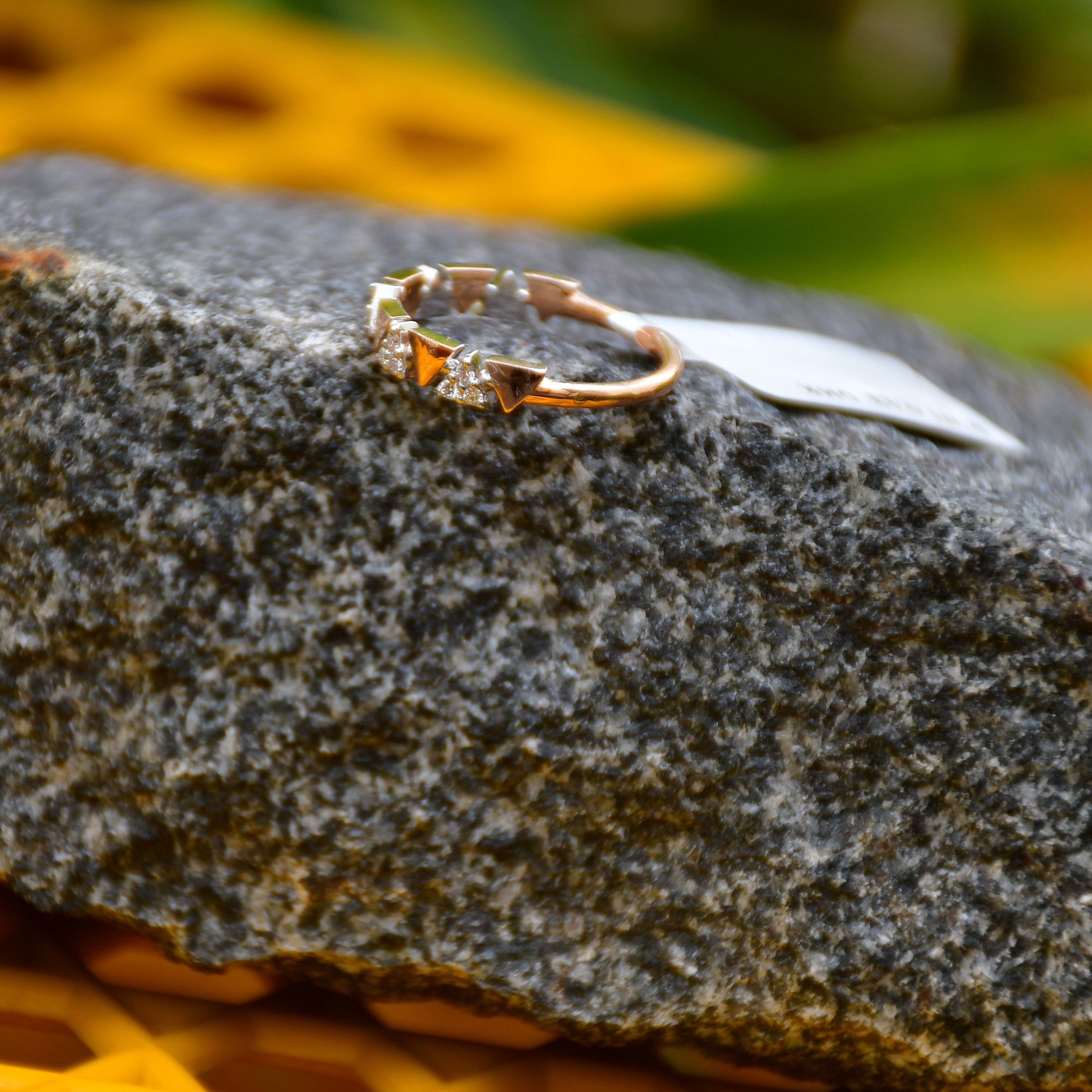 Gold diamond ring on a textured stone surface with blurred yellow flowers in the background
