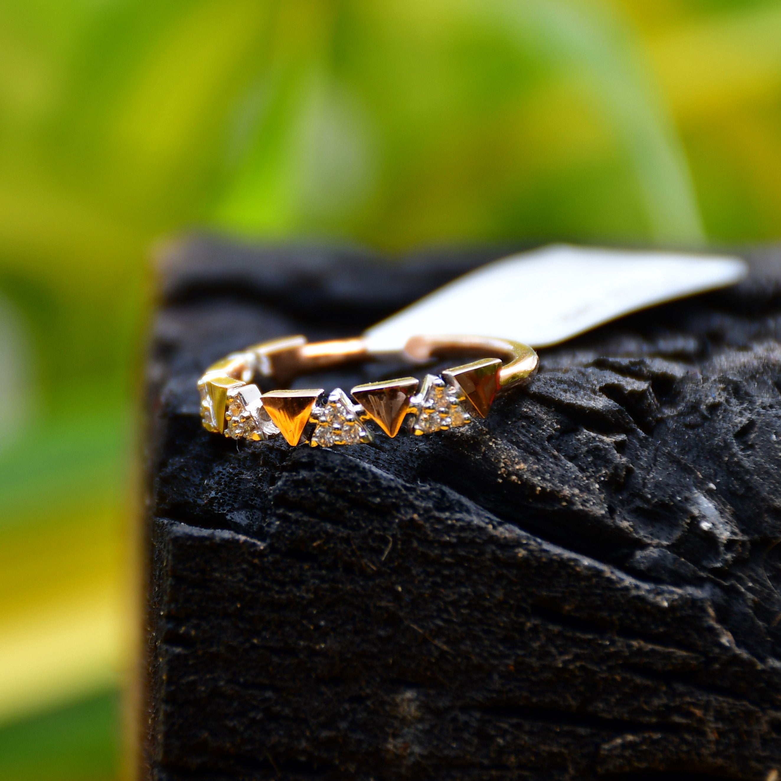 Gold ring with small diamonds on a dark stone surface with a blurred green background