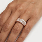 A close-up of a hand wearing a rose gold ring set with multiple rows of clear pavé diamonds.