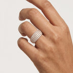 A close-up of a hand wearing a wide gold band ring set with multiple rows of small clear diamonds, photographed against a plain light background.